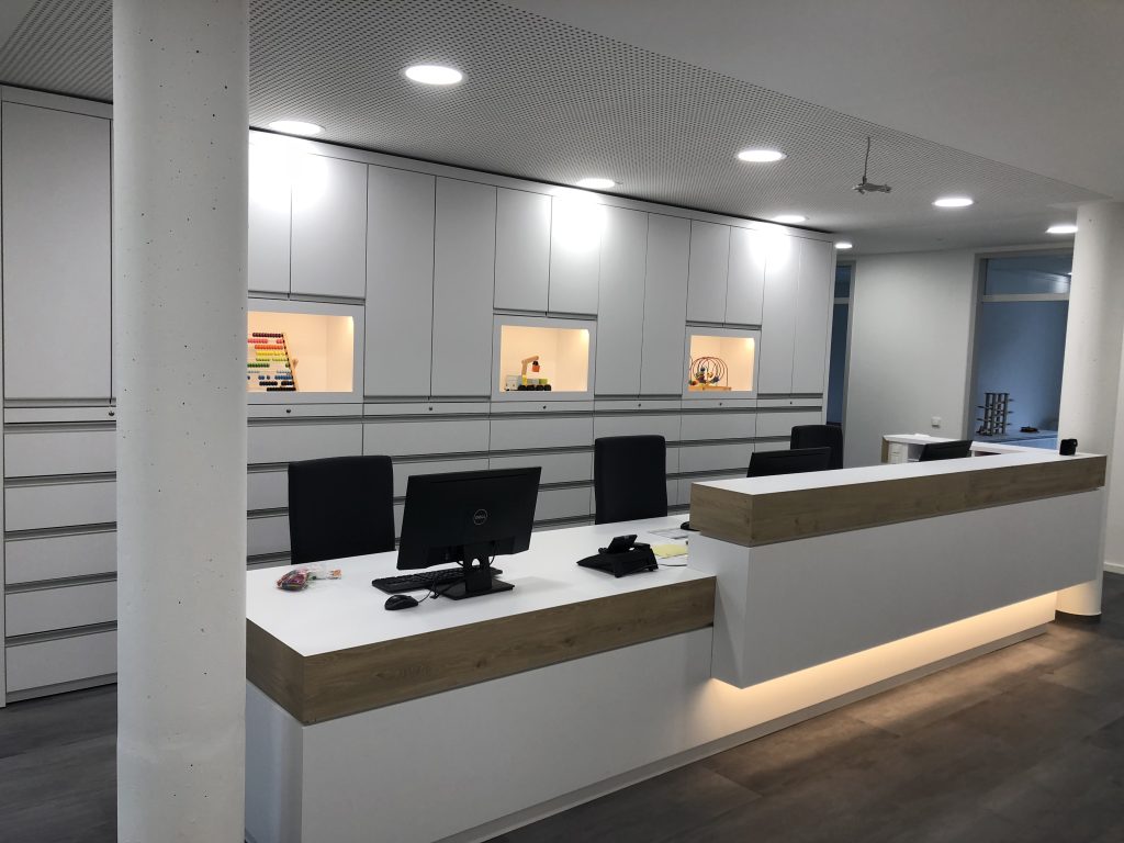 Moderner Ladenbau für Arztpraxen: Maßgefertigte weiße Empfangstheke mit Eichenholz-Elementen und indirekter LED-Beleuchtungg