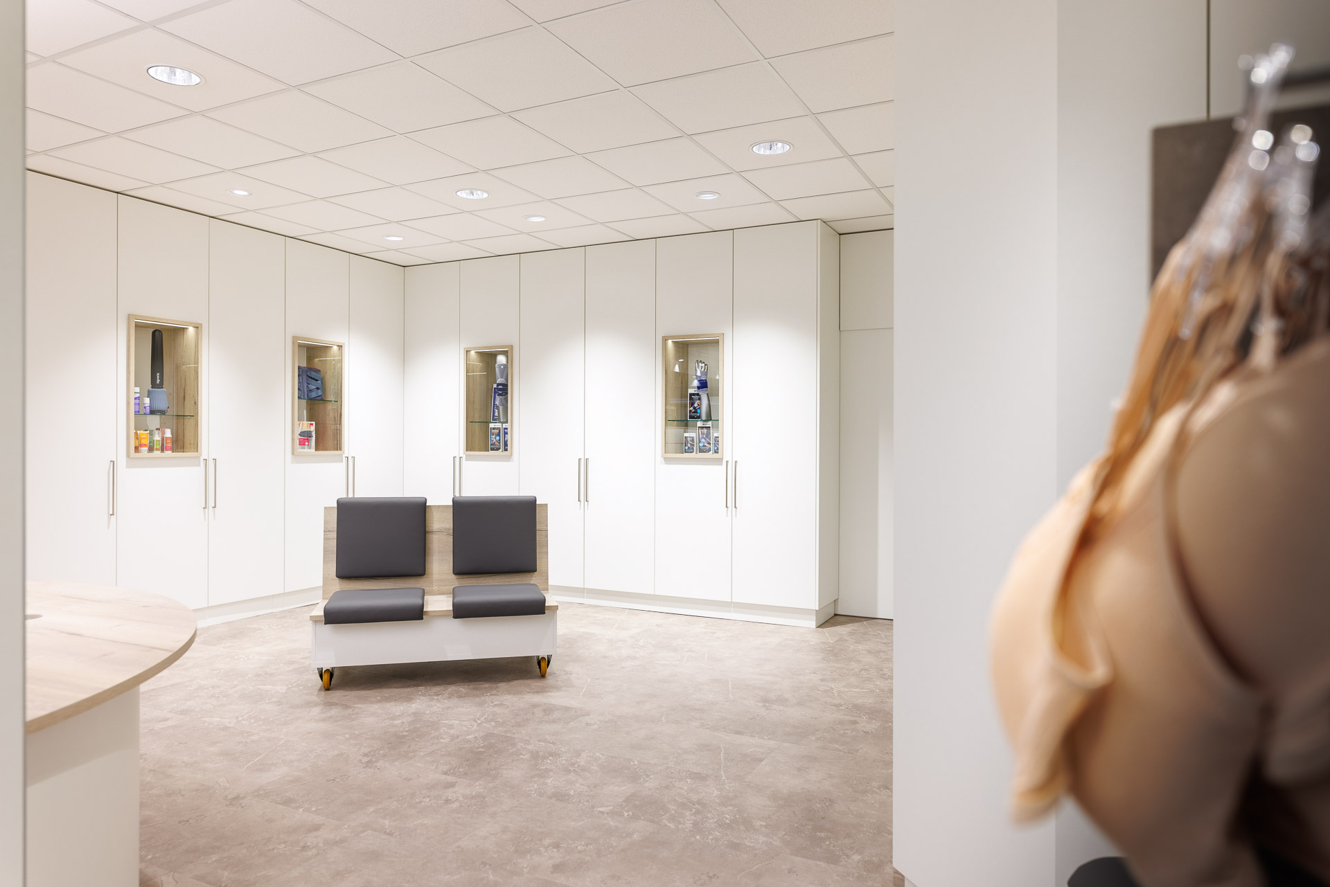 Sanitätshaus-Ansicht mit Wartebereich im Vordergrund: bequeme Sitzgelegenheit zum Hinsetzen und Anprobieren von Produkten. Im Hintergrund ein Schrank mit übersichtlich gelagerter Ware